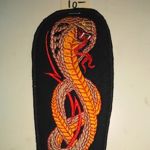 May include: Embroidered iron-on patch featuring a coiled cobra with red and orange details on a black background. The patch is shaped like a long oval.