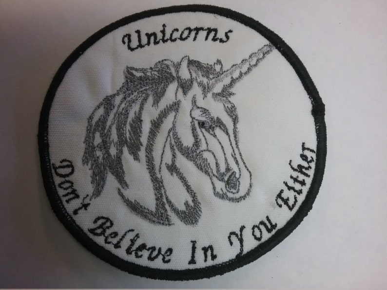May include: White embroidered patch with a black border. The patch features a silver unicorn head with the text "Unicorns Don't Believe In You Either".
