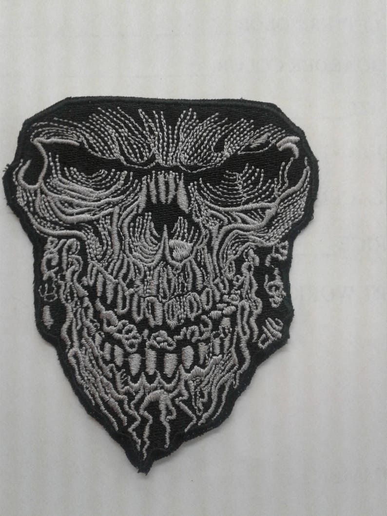 May include: A black and silver embroidered patch featuring a detailed skull design.