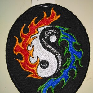 May include: A black embroidered patch with a yin yang symbol surrounded by flames on one side and water on the other. The flames are orange and red, and the water is blue and green.