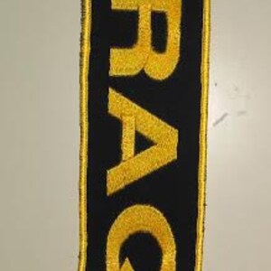 May include: Black fabric patch with a yellow embroidered word "IRAQ" on it.