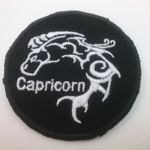 May include: Black embroidered patch with a white Capricorn zodiac symbol and the word "Capricorn" in white lettering.
