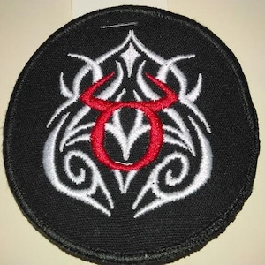 May include: A black embroidered patch with a white tribal design and a red bull's head in the center.