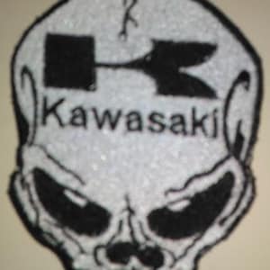May include: White skull patch with a black Kawasaki logo and a black arrow design. The skull has a detailed design with black eyes and a mouth.