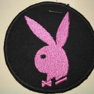 May include: A black circular patch with a pink embroidered Playboy bunny logo.