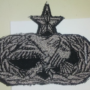 May include: A black and silver embroidered patch with a five-pointed star on top and two eagles with wings spread out below. The patch is on a white background.