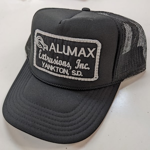 May include: Black trucker hat with a white embroidered patch that reads "ALUMAX Extrusions, Inc. YANKTON, SD."