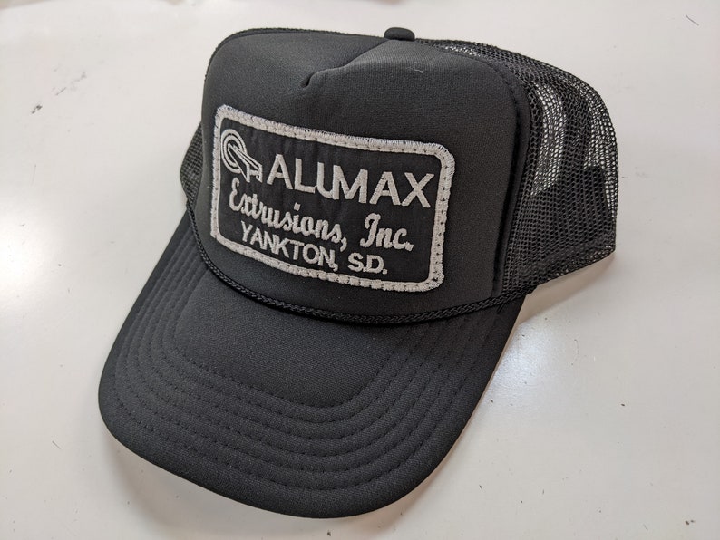 May include: Black trucker hat with a white embroidered patch that reads "ALUMAX Extrusions, Inc. YANKTON, SD."