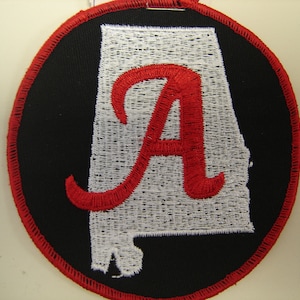 May include: A red embroidered letter "A" inside a white outline of the state of Alabama. The outline is on a black circular patch with a red border.