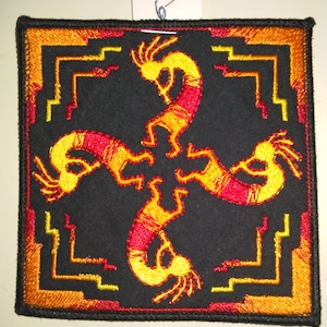 May include: Square black patch with embroidered Kokopelli figures in yellow and red. The patch has a geometric border in orange and yellow. The Kokopelli figures are arranged in a circular pattern. The patch has a white tag attached to the top.