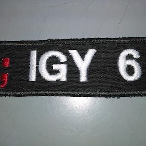 May include: Black rectangular patch with white embroidered text "IGY 6" and a red semicolon.