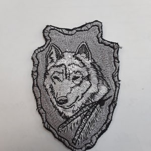 May include: A gray and black embroidered patch featuring a wolf's head in a gray and black frame.