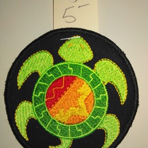 May include: A green and yellow embroidered turtle patch on a black background. The turtle has a red, orange, and yellow circle in the center of its shell.