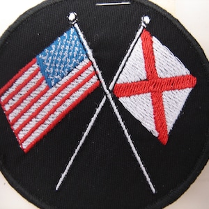 May include: A black oval patch with an embroidered American flag and an embroidered English flag crossed over each other.