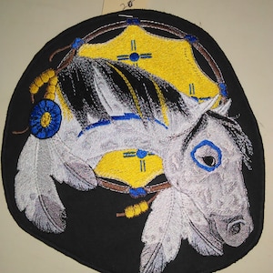 May include: Embroidered patch featuring a white horse head with blue eyes and a yellow and blue dreamcatcher. The patch is on a black background.