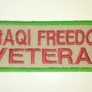 May include: A tan fabric patch with a green border. The patch has red embroidered text that reads "IRAQI FREEDOM VETERAN".