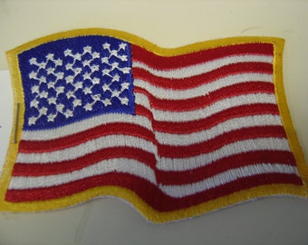May include: A red, white, and blue embroidered American flag patch with a yellow border. The flag is waving in the wind.