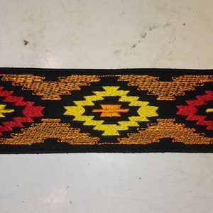 May include: A black fabric patch with a repeating geometric pattern in orange, red, and yellow.