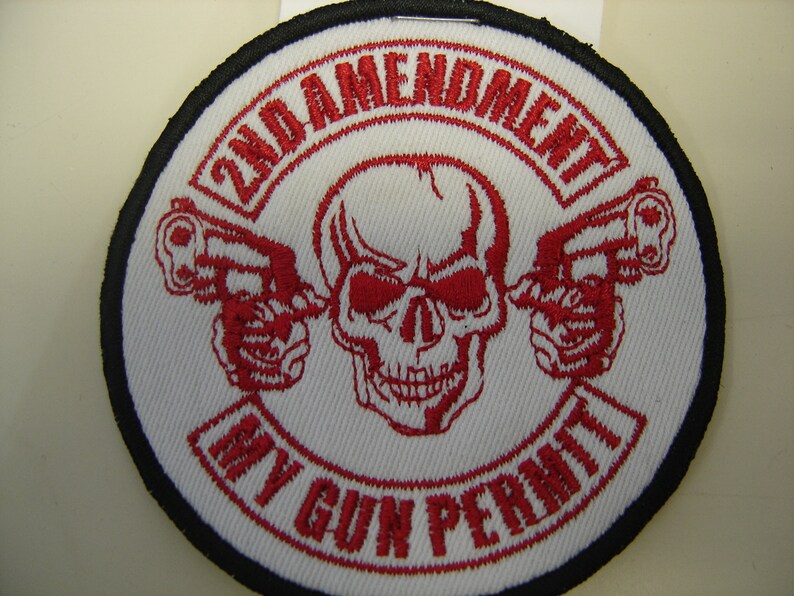 May include: A white embroidered patch with a red skull and crossbones design. The text "2nd Amendment My Gun Permit" is written in a red circular banner around the skull and crossbones.