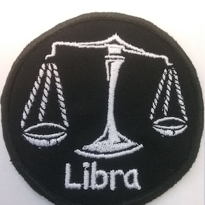 May include: White embroidered Libra zodiac sign on a black circular patch. The sign features a scale with two hanging pans.