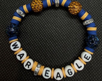 Può includere: Un braccialetto elastico con perline piatte blu e gialle, perline con lettere bianche che compongono WAR EAGLE, due sfere color ambra incastonate di strass, due sfere blu scuro incastonate di strass e tre distanziatori in strass color argento.