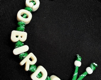 Può includere: Un portachiavi realizzato con una corda in paracord verde infilata con perline a lettera in plastica color bianco sporco che compongono la parola GOBIRDS. La corda è fissata con un anello in metallo dorato e termina con due piccole perline.
