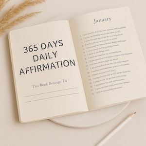 May include: Open notebook with the text "365 DAYS DAILY AFFIRMATION" on the left page. The right page is open to January with affirmations. A white pencil rests on the bottom right corner.