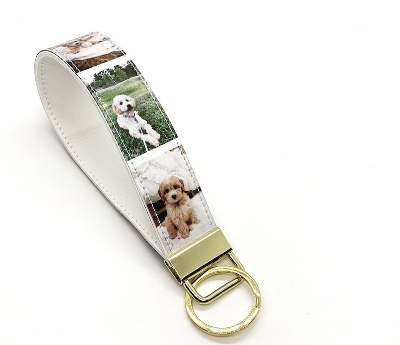 May include: White leather keychain with a gold key ring. The keychain features a strip of fabric with four photos of a small, light brown dog.
