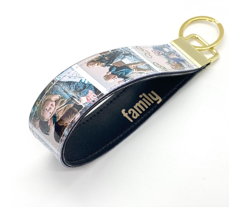 May include: A black leather keyring with a clear plastic strip featuring multiple photos of a family. The keyring has a gold metal ring and the word "family" is embossed in gold on the leather.