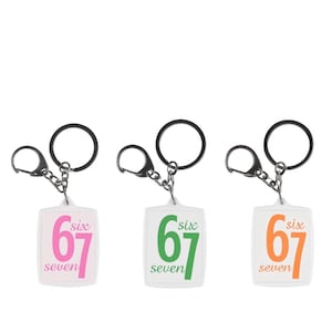 May include: Three keychains with white rectangular tags. Each tag features the number "67" and the word "six" above and "seven" below. The keychains have different color schemes: pink, green, and orange.