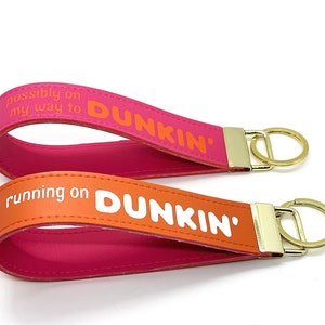 May include: Two pink and orange leather keychains with gold key rings. The keychains have the text "possibly on my way to DUNKIN'" and "running on DUNKIN'" printed on them.