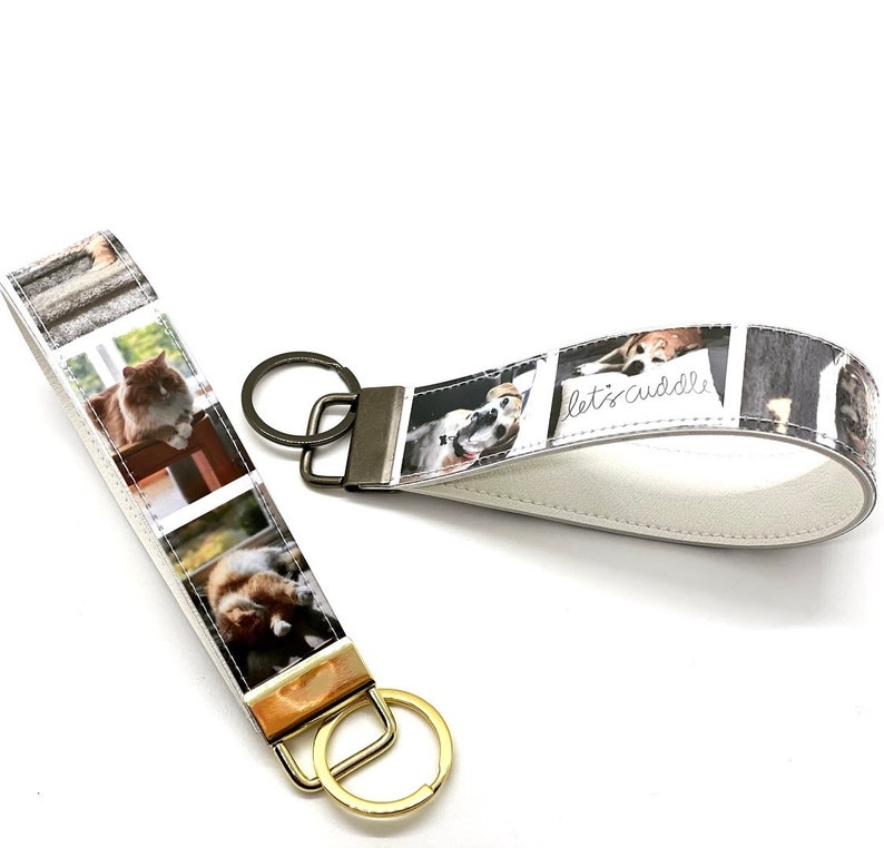 May include: Two keychains with white leather straps and metal rings. One keychain features a white background with a collage of photos of dogs and cats. The other keychain features a white background with a collage of photos of cats. The text "let's cuddle" is printed on the dog keychain.