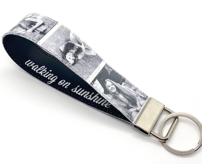 May include: Black and white photo keychain with a black leather strap. The strap has the text "walking on sunshine" printed on it. The keychain has a silver metal ring.