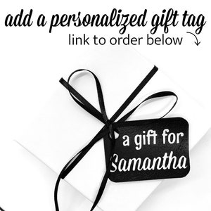 May include: A white gift box with a black ribbon and a black gift tag that says "a gift for Samantha".
