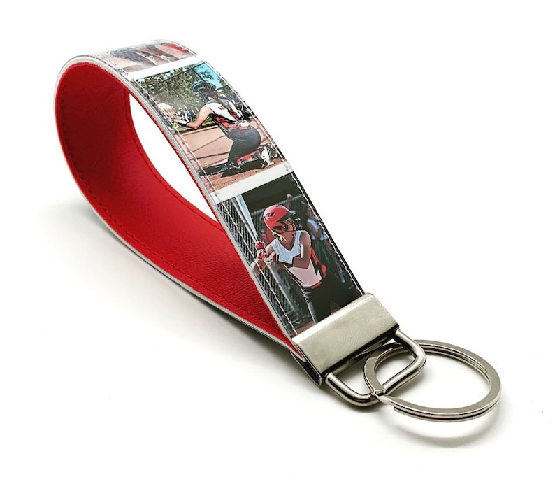 May include: Red leather keychain with a photo strip design featuring a girl playing baseball. The keychain has a silver metal key ring.