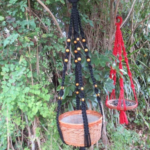 May include: Two macrame plant hangers, one black with wooden beads and a brown woven pot, and one red with a brown woven dish.