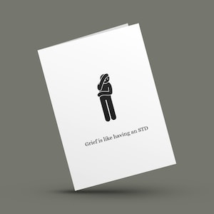 May include: White greeting card with a black stick figure and the text "Grief is like having an STD." The stick figure is holding their head. The card is angled against a gray background.