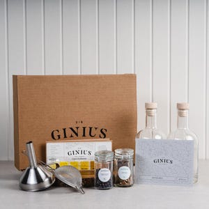 May include: A gin-making kit featuring a brown cardboard box, two clear glass bottles, and two small glass jars. The kit includes a stainless steel funnel and strainer, and a card with the text "GINIUS".