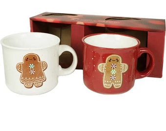 May include: Two ceramic mugs with gingerbread person designs. One mug is white with a gingerbread person design and the other mug is red with a gingerbread person design and white speckles.