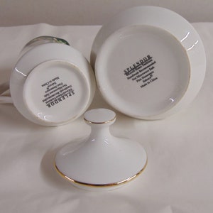 May include: White porcelain creamer and sugar bowl set with gold trim. The creamer has a handle and a floral design. The sugar bowl has a lid with a gold trim. The set is labeled "SPLENDOR" and "Sakura".
