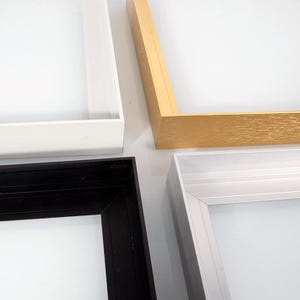 Puede incluir: Primer plano de cuatro marcos de fotos de diferentes colores. Los marcos son blancos, dorados, negros y plateados. Los marcos están vacíos, con espacio blanco en el centro. Los marcos son de madera o metal.