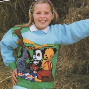 Puede incluir: Un suéter azul claro con un diseño de personaje de Sooty. El suéter tiene cuello y puños verdes, y se combina con pantalones azul claro. La imagen también incluye el texto "SOOTY" y "CHARACTER COLLECTION".