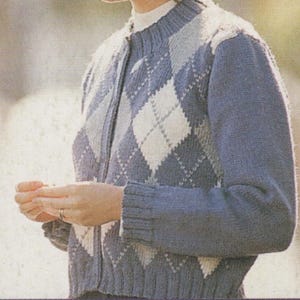 Può includere: Un cardigan blu con un motivo a rombi bianco e grigio. Il maglione ha colletto, polsini e orlo a coste. Il cardigan è abbottonato e sembra essere realizzato in morbido materiale a maglia.