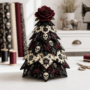 May include: A decorative fabric tree featuring a layered, quilted design with a pattern of white skulls and red roses on a black and cream background. The tree is topped with a single, large, deep red fabric rose, creating a conical shape.