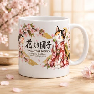 May include: A white ceramic mug featuring a calico cat wearing a pink floral kimono, holding a dango skewer. The design includes cherry blossom branches, gold clouds, and the text "花より団子 HANA YORI DANGO - Dumplings Over Flowers - Choose what truly matters."