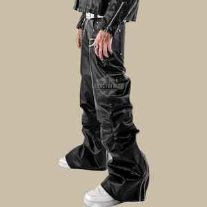 Puede incluir: Pantalones de cuero negro con un diseño único, con un bajo acampanado y detalles de cremallera. Los pantalones tienen una textura ligeramente arrugada y se combinan con zapatillas blancas. El texto "LEGACYOFHIDE" es visible.