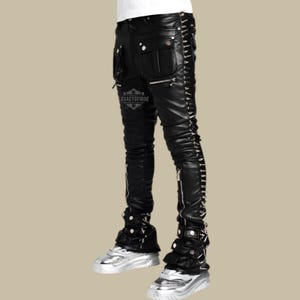 Puede incluir: Pantalones de cuero negro con múltiples bolsillos, cremalleras y tachuelas plateadas en los laterales. Los pantalones tienen un diseño apilado en los tobillos y se combinan con zapatillas plateadas. El texto "LEGACYOFHIDE" es visible.