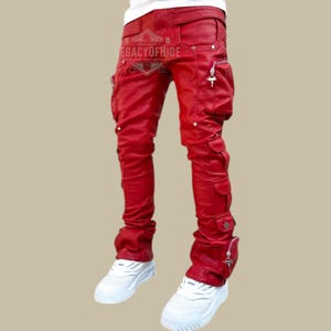 Puede incluir: Pantalones de cuero rojos con múltiples bolsillos y herrajes plateados. Los pantalones tienen un diseño apilado en los tobillos y un cinturón. El texto "LEGACYOFHIDE" es visible en el cinturón. Se combinan con zapatillas blancas.