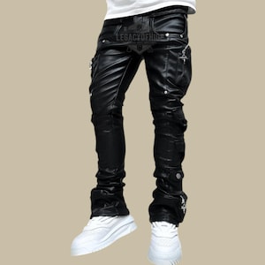 Puede incluir: Pantalones de cuero negro con múltiples bolsillos y cremalleras. Los pantalones tienen un diseño apilado en los tobillos y presentan el texto "LEGACYOFHIDE" en la cintura. La persona lleva zapatillas blancas.