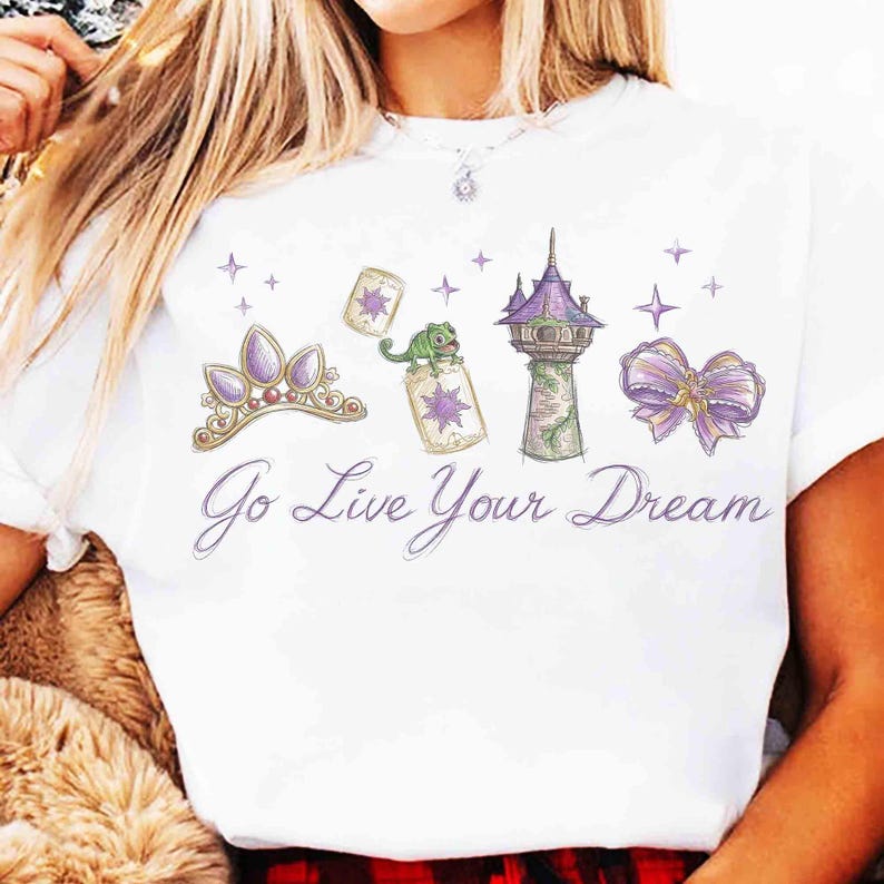 Może przedstawiać: Biała koszulka z nadrukiem przedstawiającym fioletową tiarę, lampiony, kameleona, wieżę i kokardę. Tekst "Go Live Your Dream" jest napisany kursywą. Projekt jest w kapryśnym, kresk&oacute;wkowym stylu.